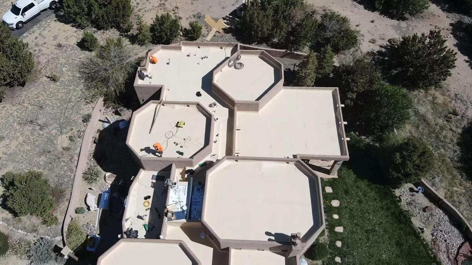 Aerial view of a beige house roof with skylights, surrounded by desert trees and shrubs.
