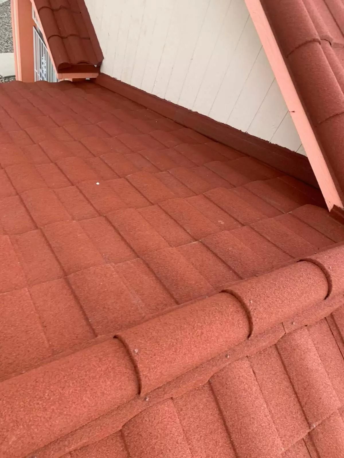 Red roof tiles beside a white wall and window on a sloped rooftop.
