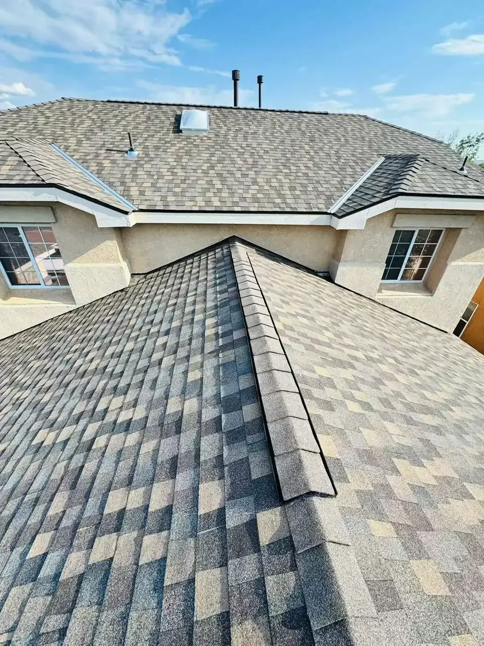 Roof shingles on a residential house, showing a central ridge and skylight under a cloudy sky