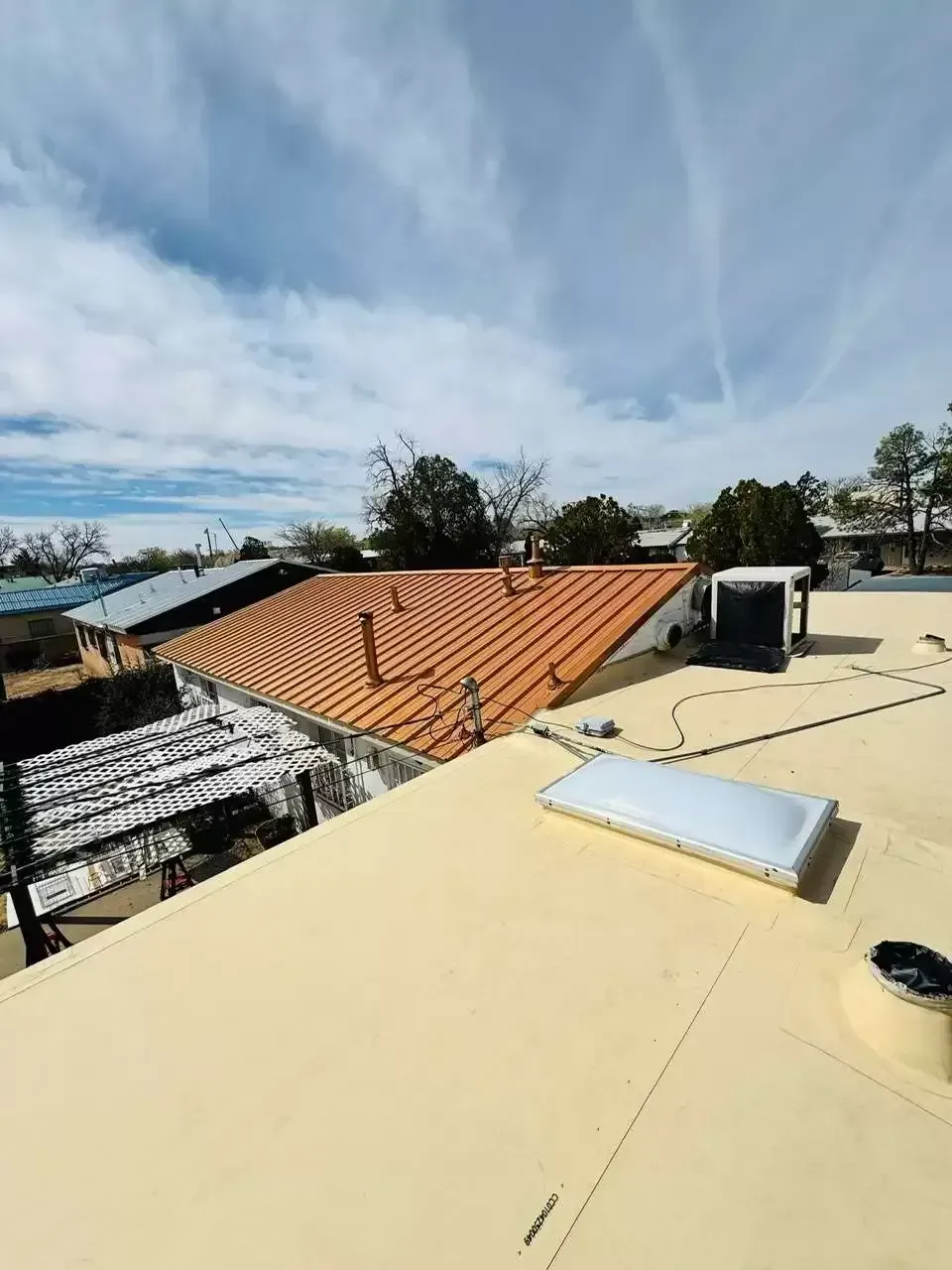 Rooftop view with solar panels, a skylight, and nearby orange-tiled roofs under a blue sky