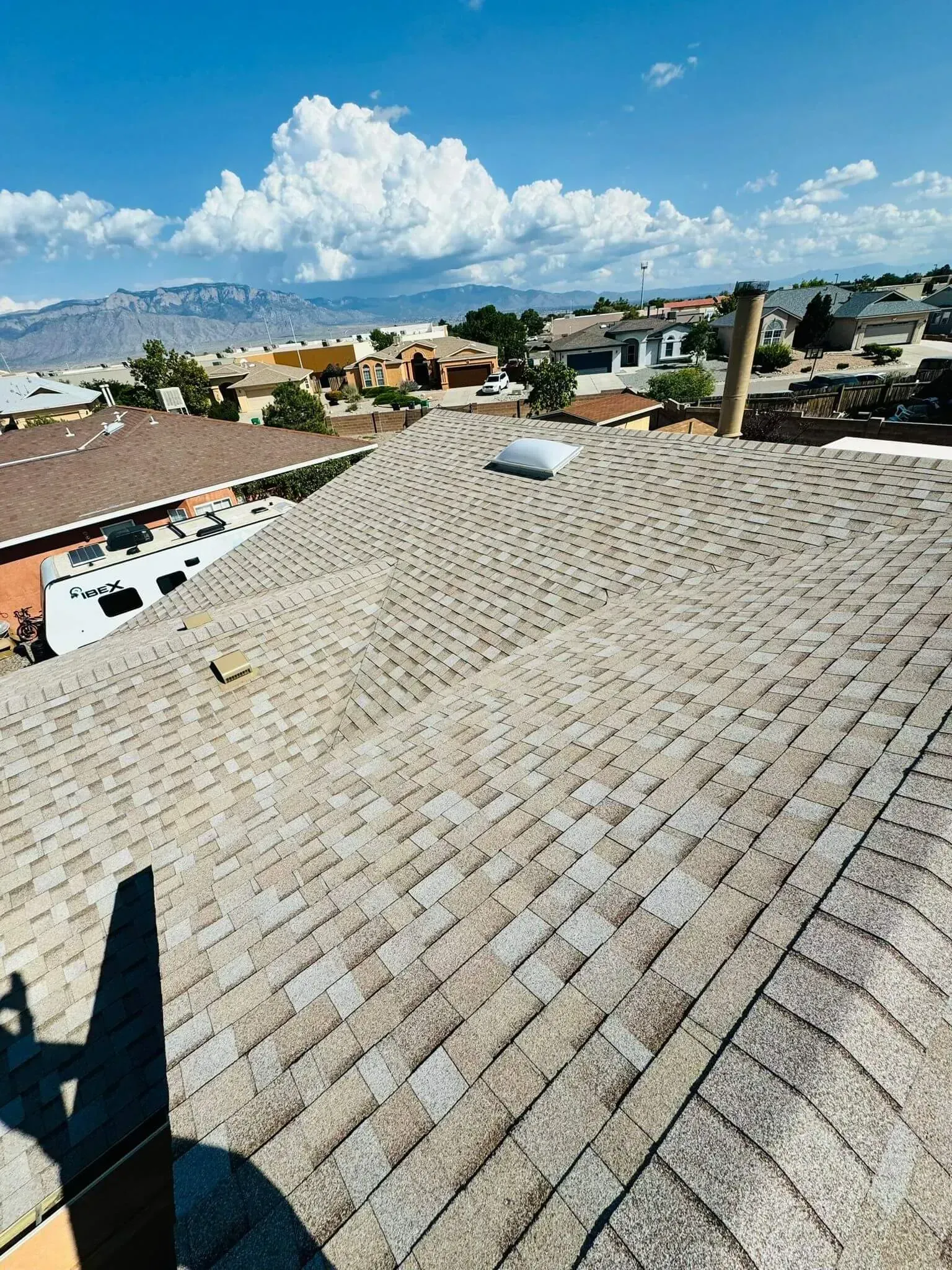 Rooftop view over houses and distant mountains under a bright blue sky with clouds