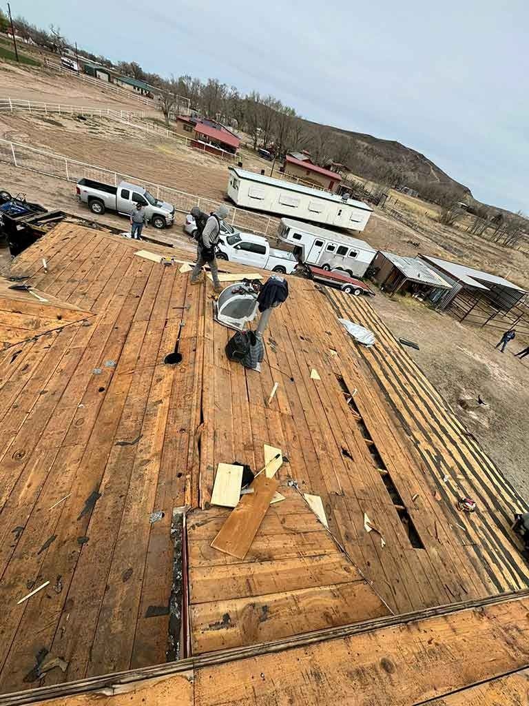 Workers on a rusted ship deck beside trucks and a large white trailer on a hillside construction site
