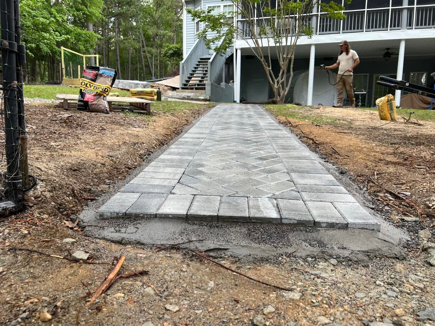 Long gravel trench lined with black fabric beside a house, bordered by mulch and trees.