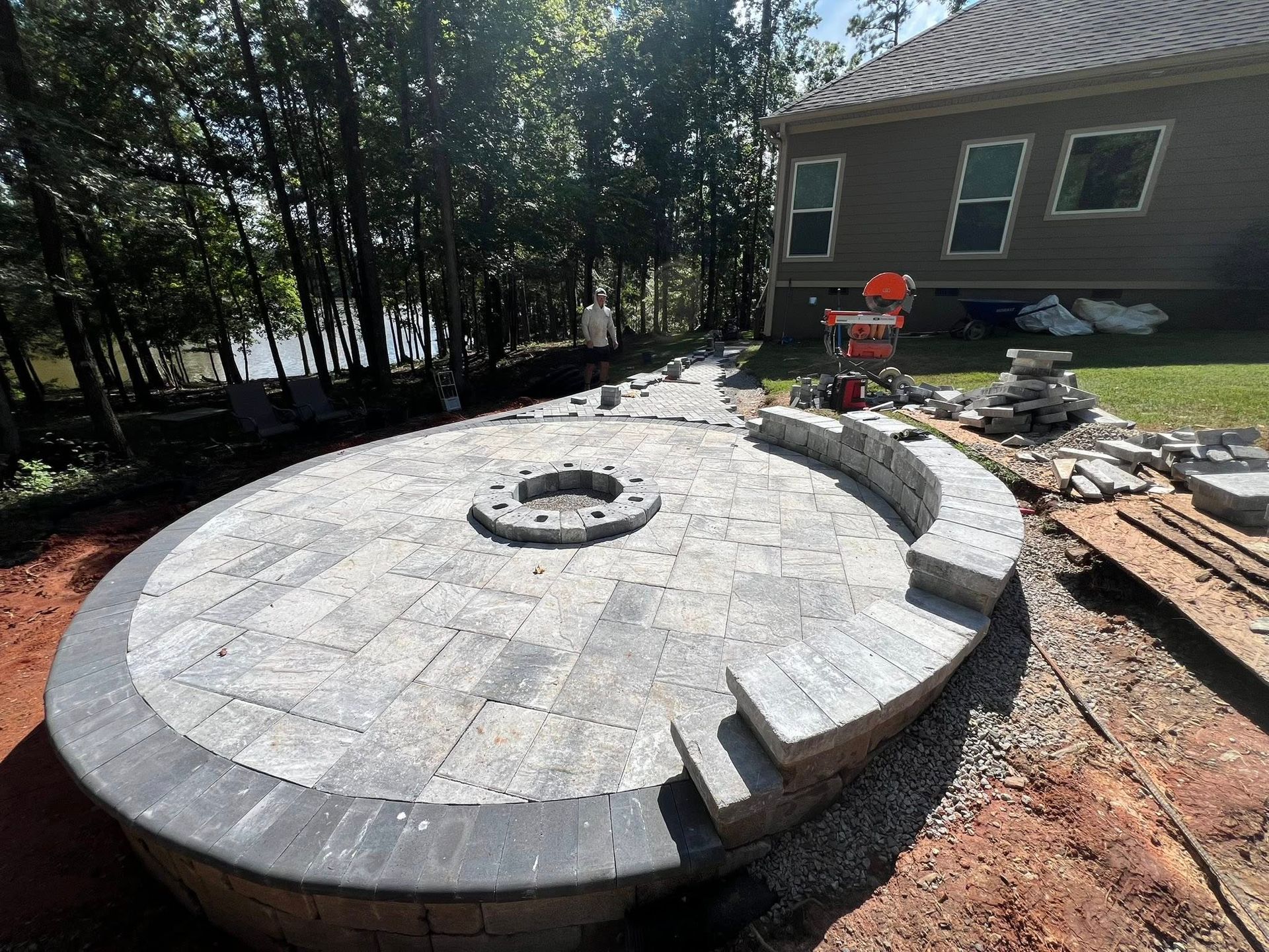 Workers paving a curved stone patio around a fire pit in a wooded backyard