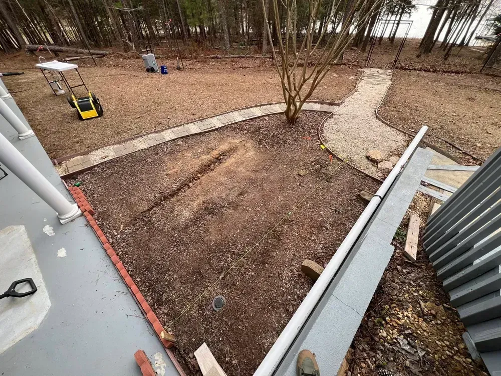 Backyard with bare ground, stone paths, a small yellow swing, and trees in the background