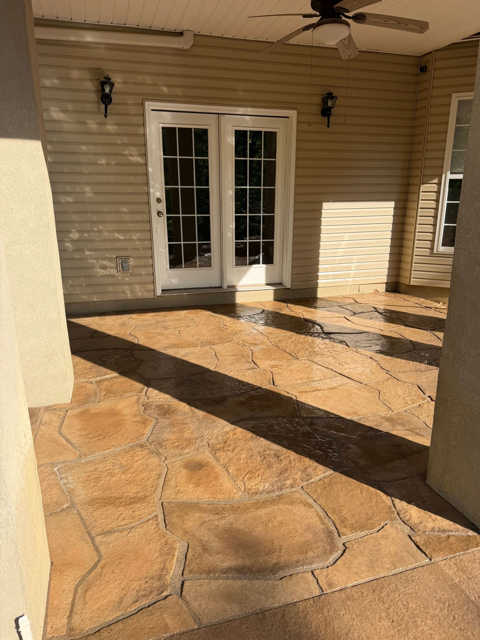 Sunlit stone patio with double French doors and strong shadows against a beige house.