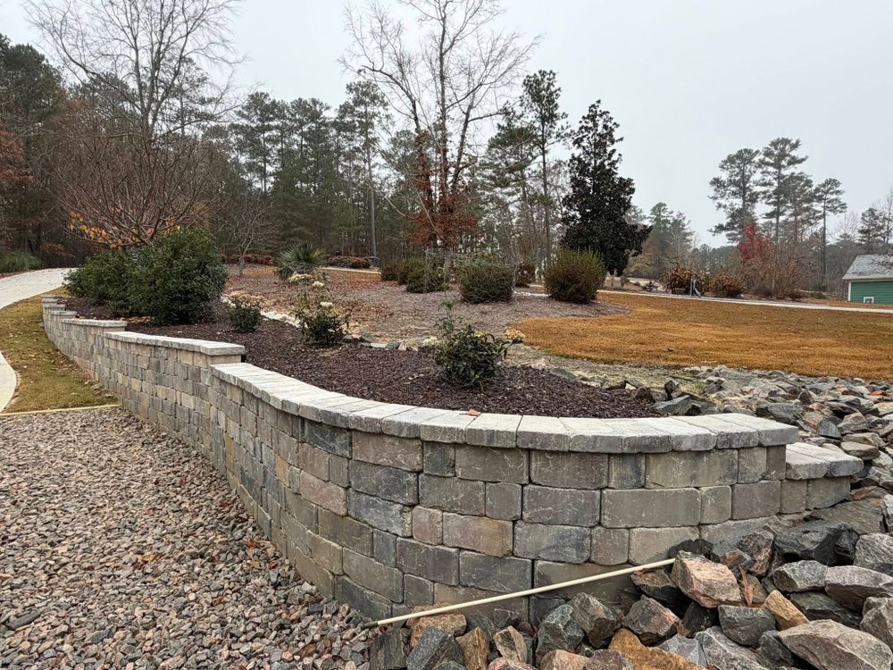 Stone retaining wall bordering a mulched garden bed and gravel path in a landscaped yard