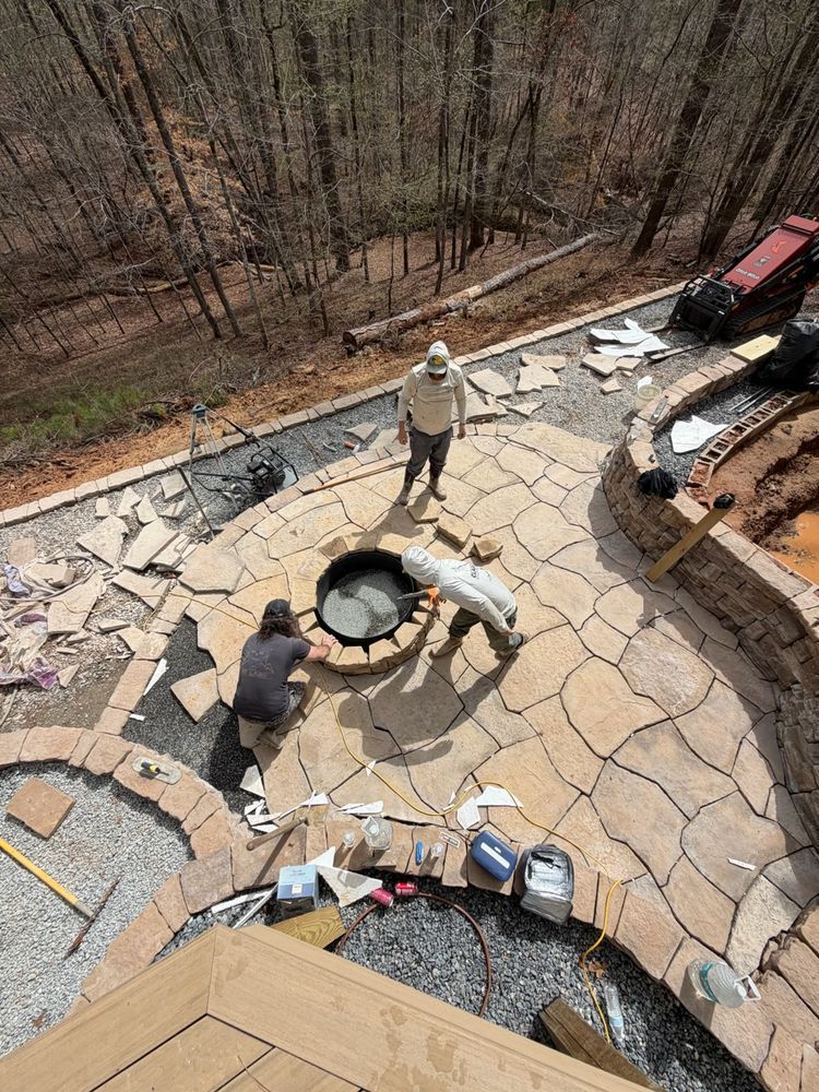 Workers paving a curved stone patio around a fire pit in a wooded backyard