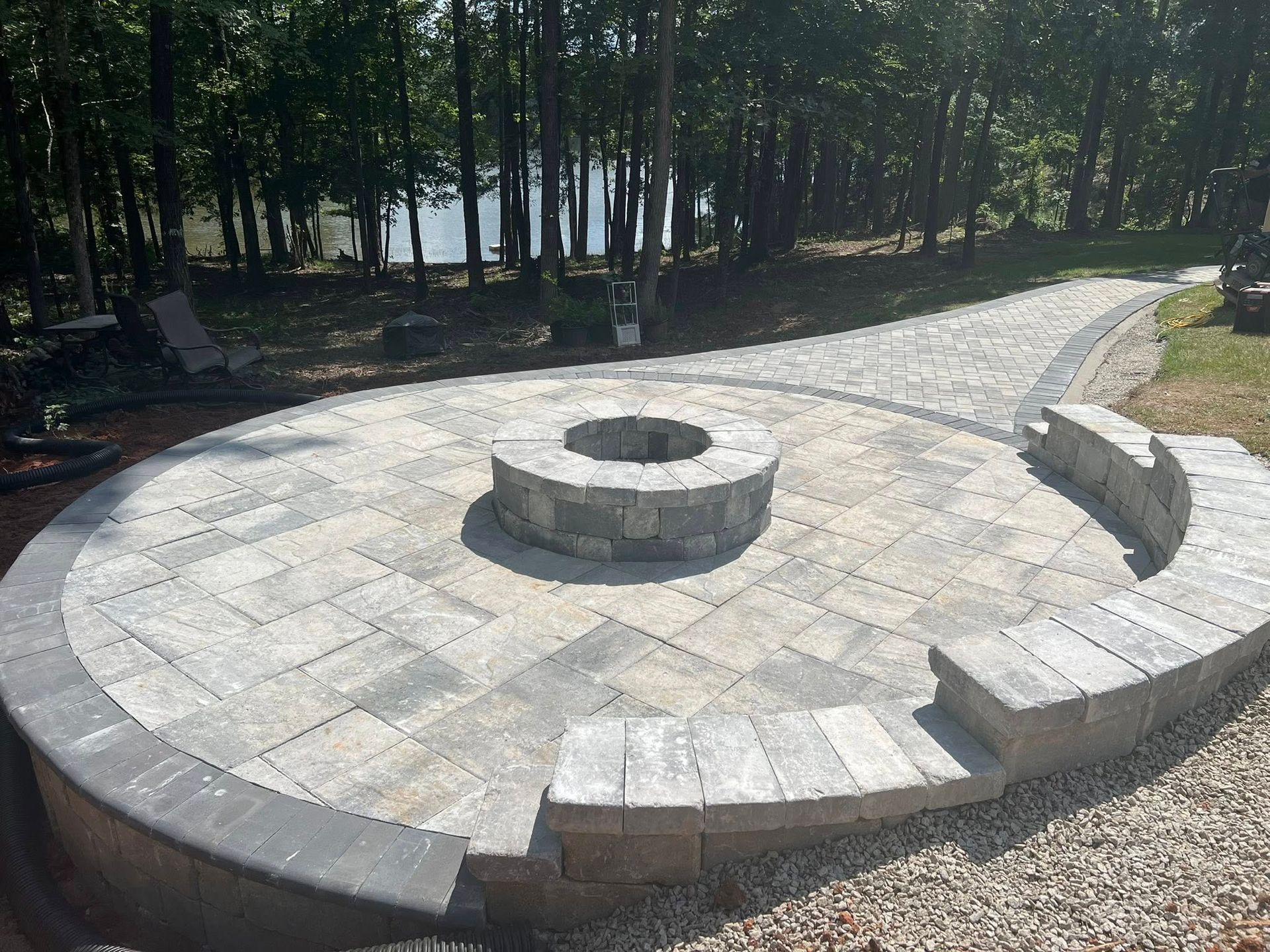 Circular stone fire pit with curved benches on a gravel patio in a wooded park area