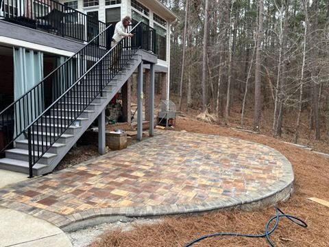 House deck with exterior stairs opening onto a curved stone patio beside woods