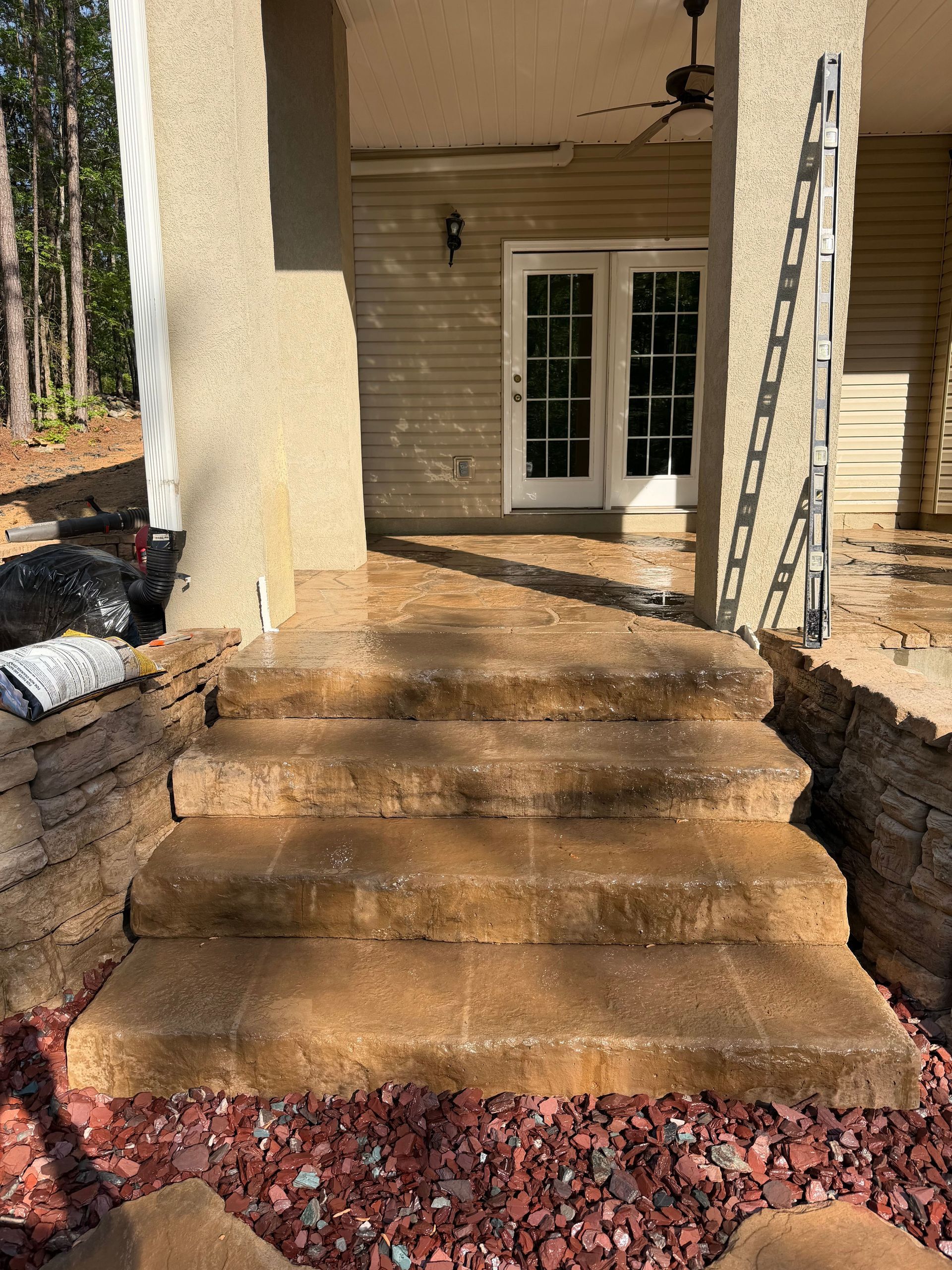 Front steps of a beige house with white double doors, flanked by stone walls and a ladder on the right.