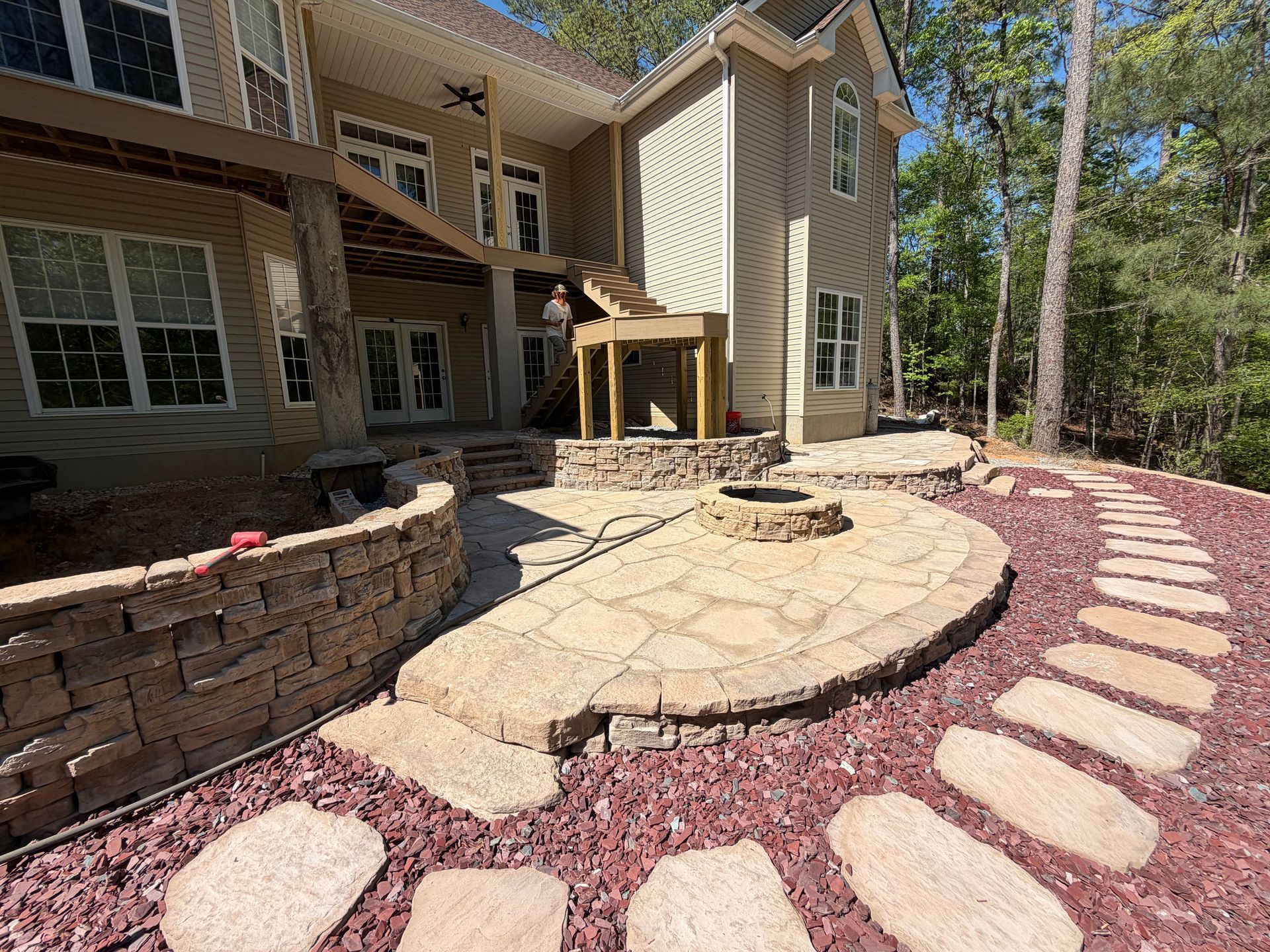 Backyard patio with curved stone walkway, circular fire pit, and house exterior amid trees