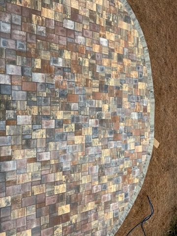 Circular mosaic tabletop with multicolored square tiles on a brown surface; black cable visible nearby