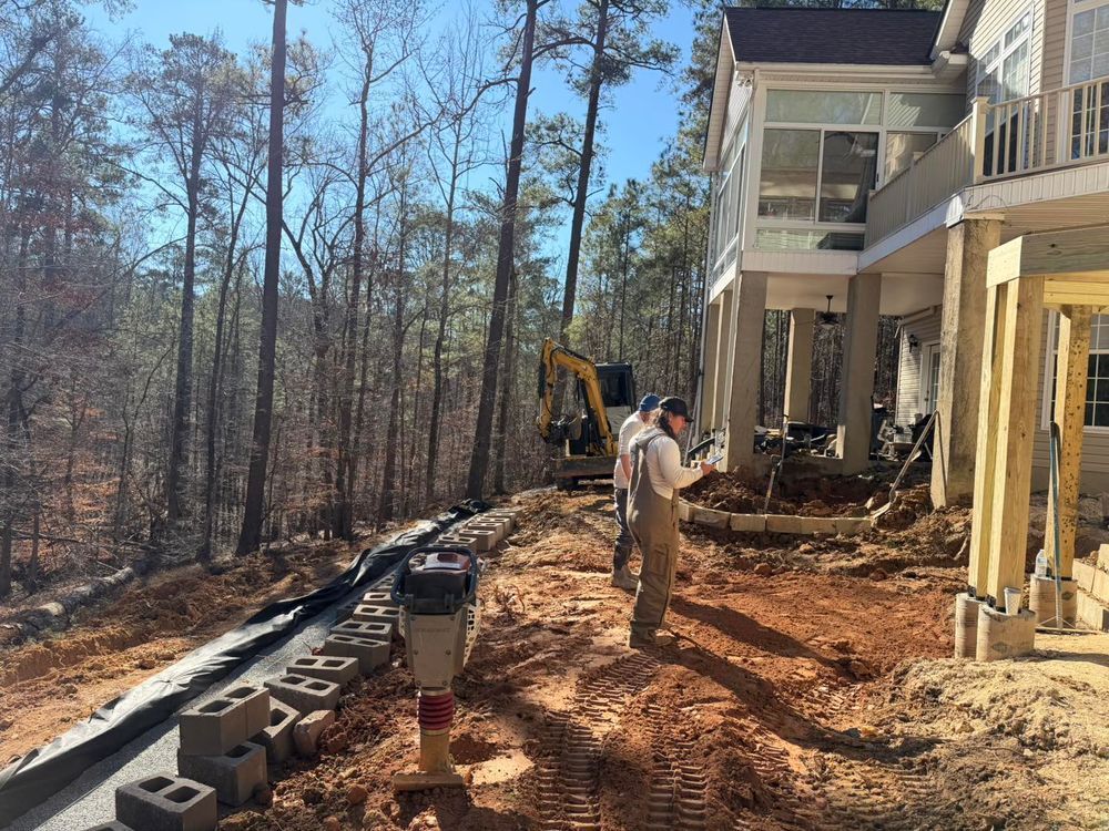 Workers and excavator on muddy construction site beside a house in a wooded area