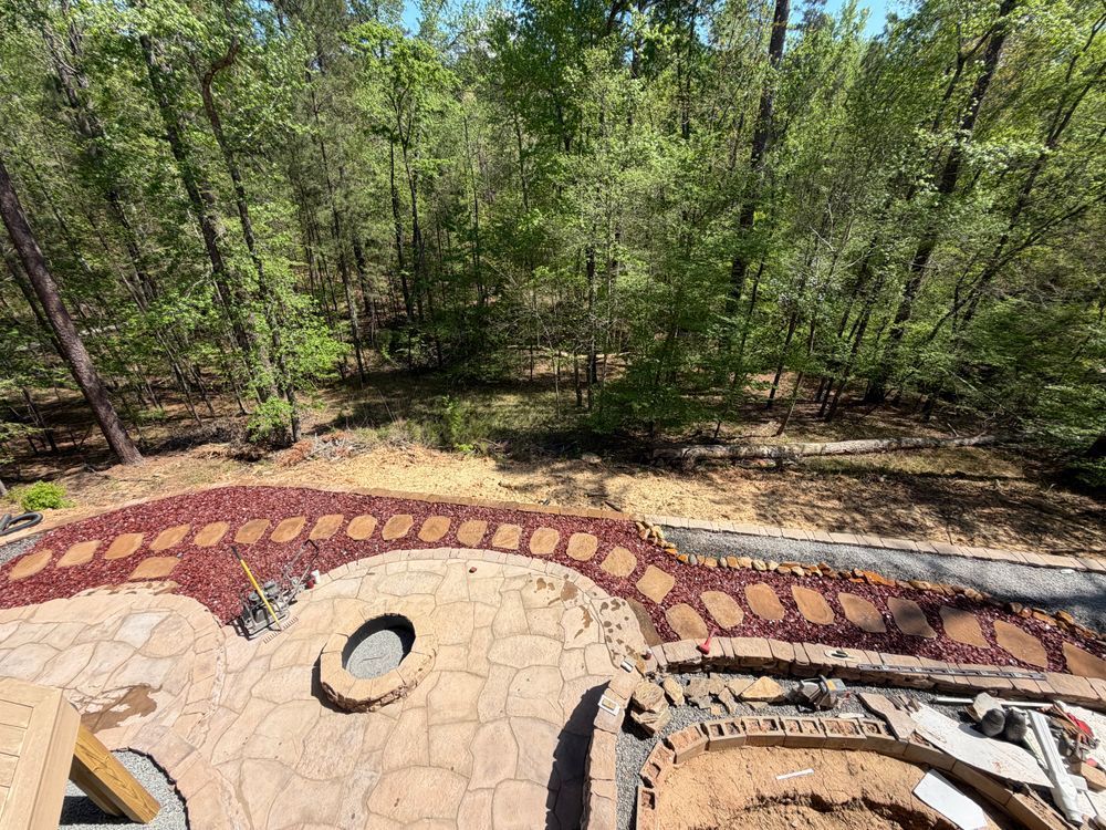 Stone patio with circular fire pit in front of a wooded backyard