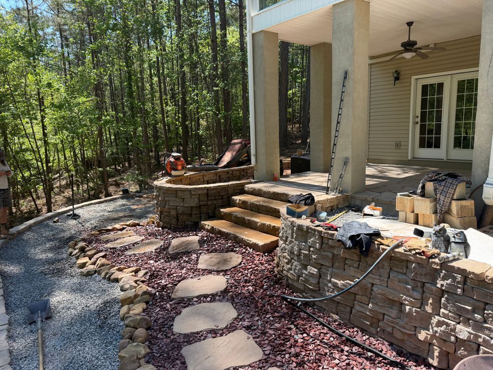 Backyard patio with stone steps, stepping-stone path, and wooded landscaping beside a house