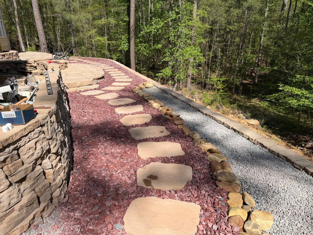 Curved garden path with stepping stones and red gravel beside a stone wall in a wooded area