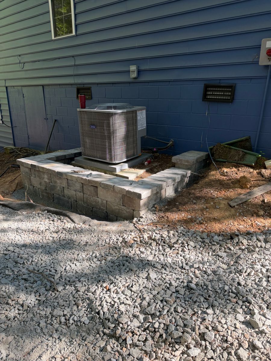 Outdoor HVAC unit on a concrete pad beside a blue house wall, surrounded by gravel.