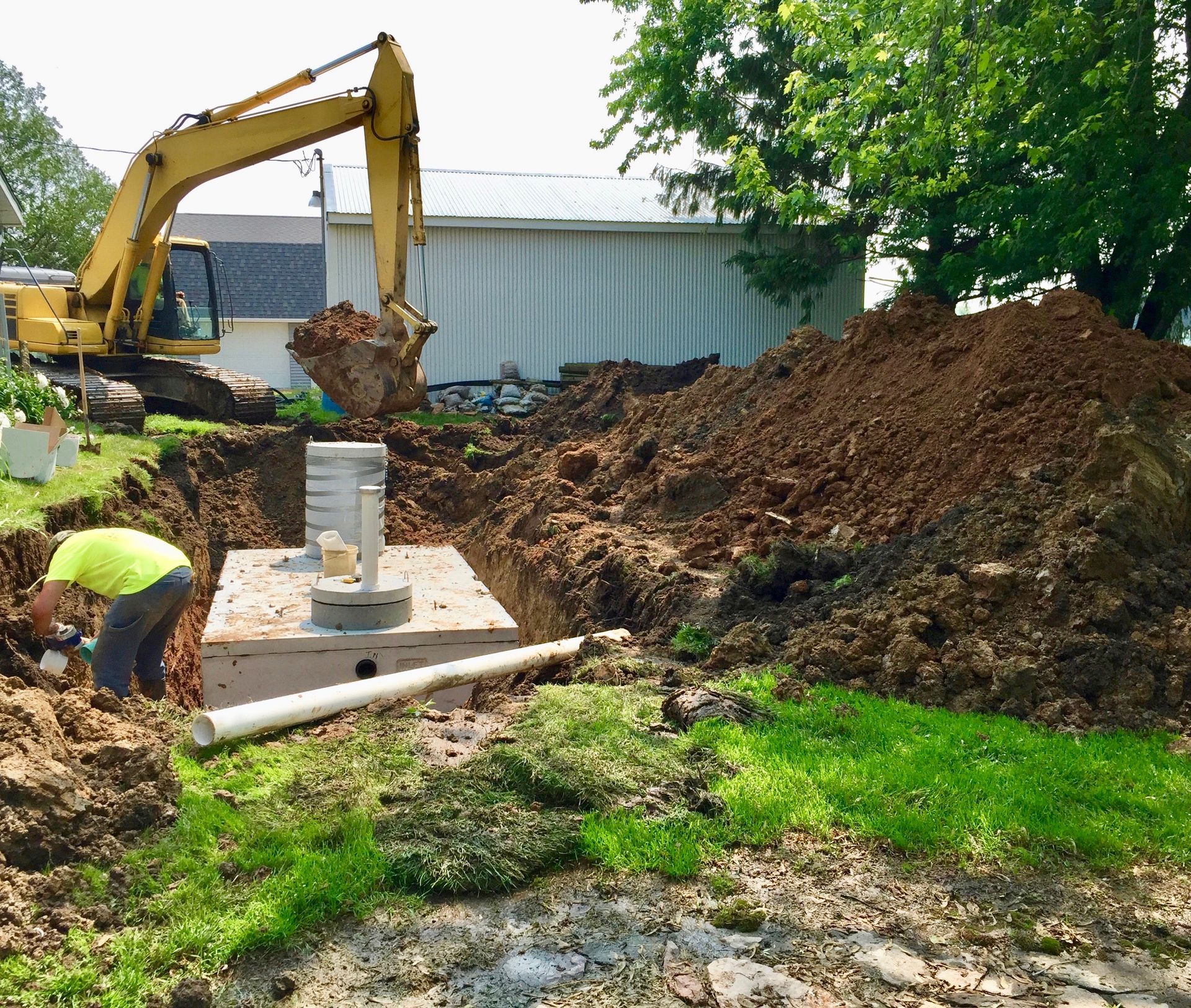 Construction site with excavator, workers, and soil piles beside a concrete foundation slab