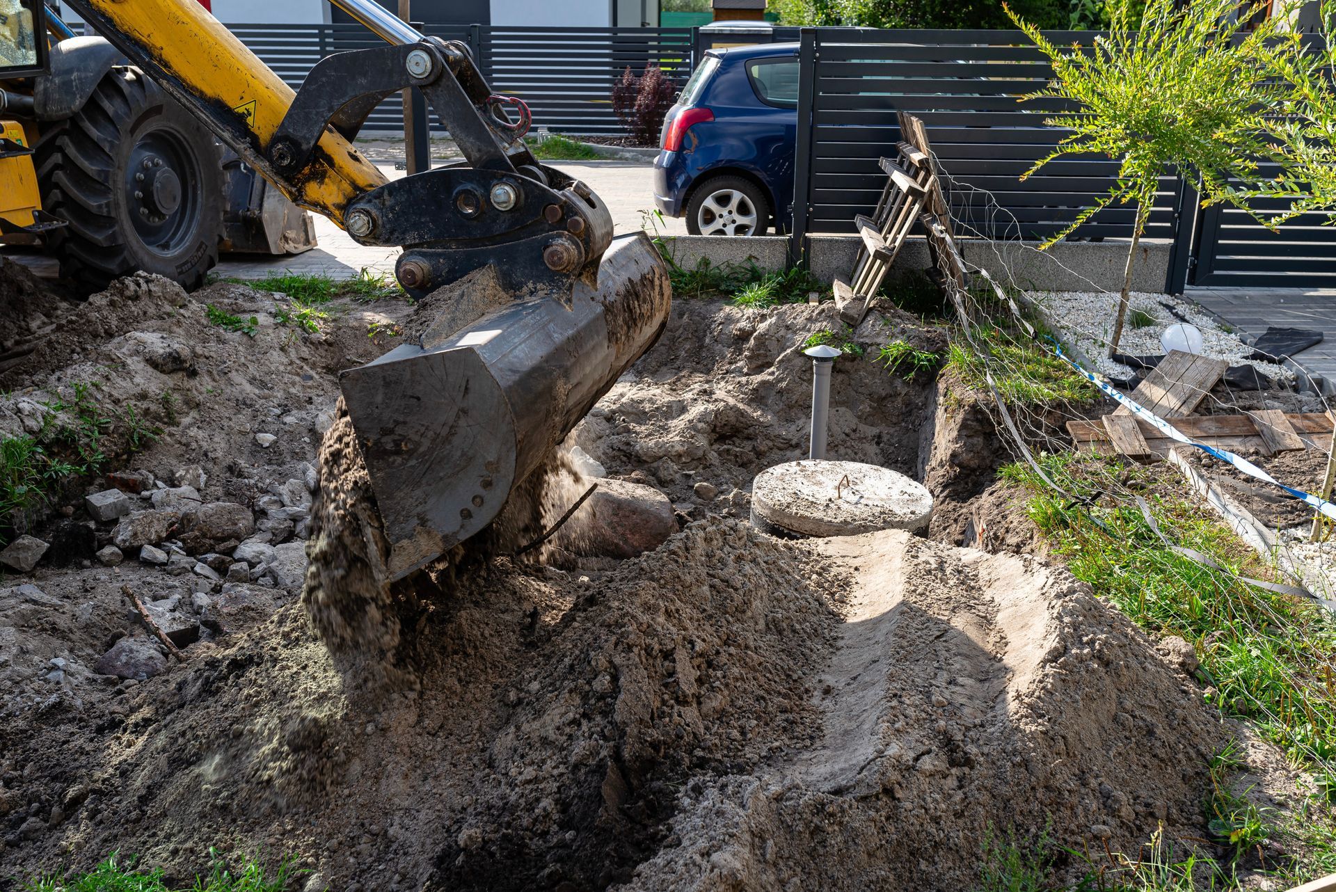 Excavator digging a large hole in a backyard, with dirt piles and a small fence nearby.