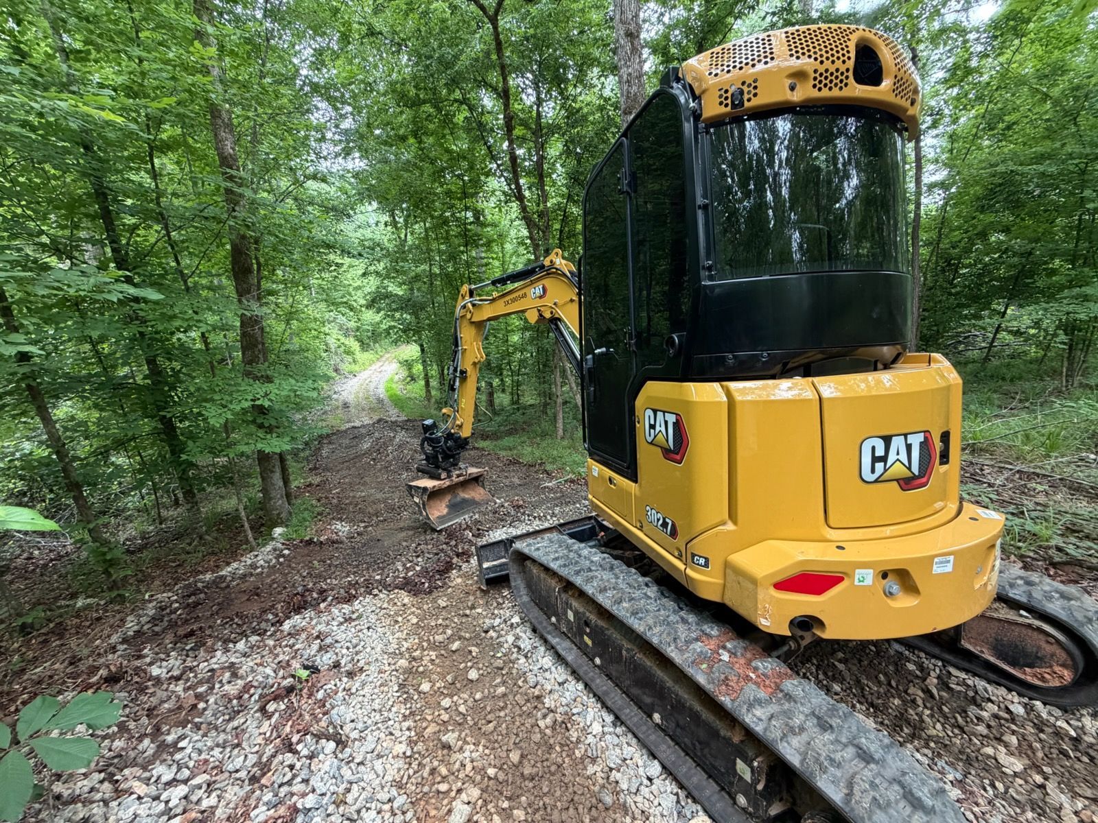 Yellow CAT excavator on tracks clearing a forest path among trees