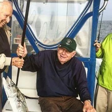 Two people on a boat, one holding a fishing rod with a caught fish, while the other sits and smiles.