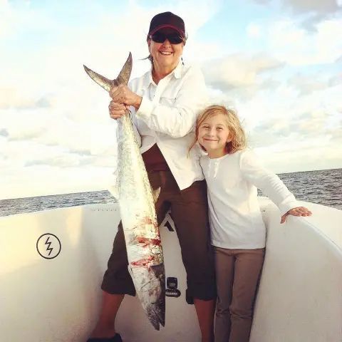 A person holding a large caught fish next to a young person on a boat on the water.