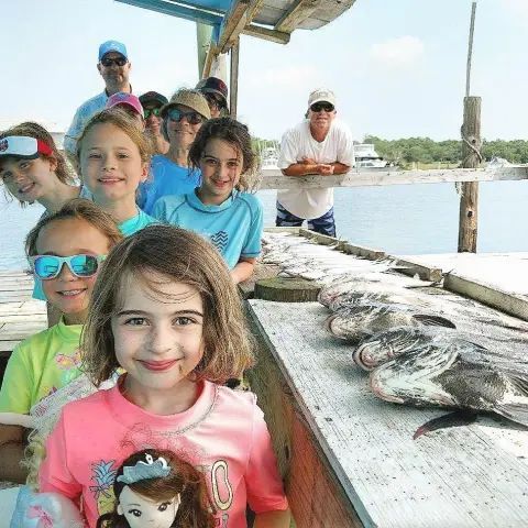 A group of people standing on a dock with a row of caught fish laid out on a wooden table.