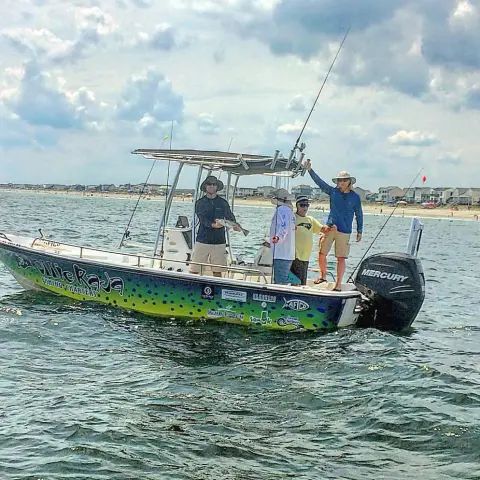 Four people on a green, yellow, and black fishing boat in the ocean, with one person holding up a fish.