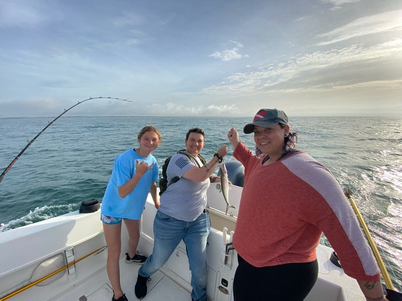 Three people on a boat in the ocean, one holding a freshly caught fish, smiling toward the camera.