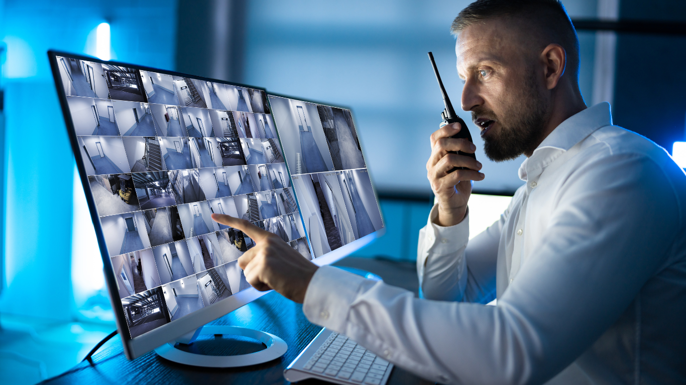 A man is talking on a walkie talkie while looking at a security system.