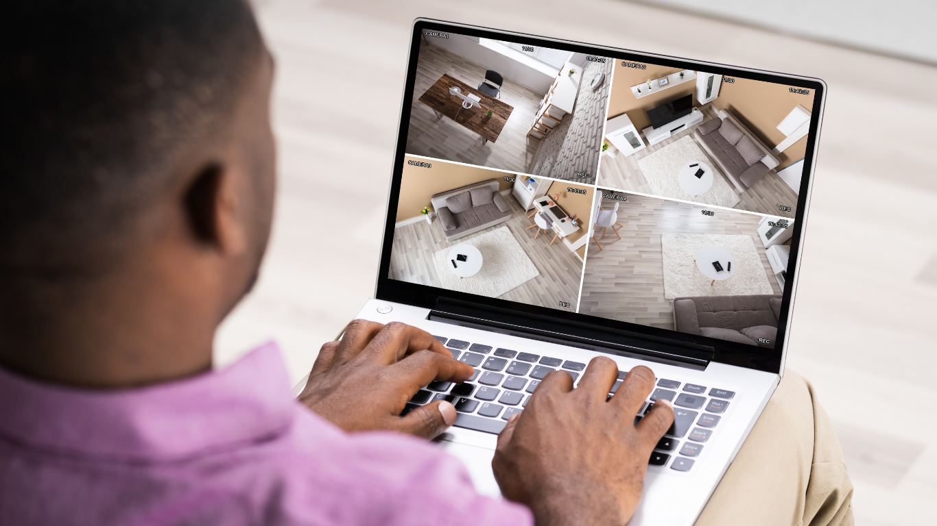 A man is using a laptop computer to view video surveillance footage.
