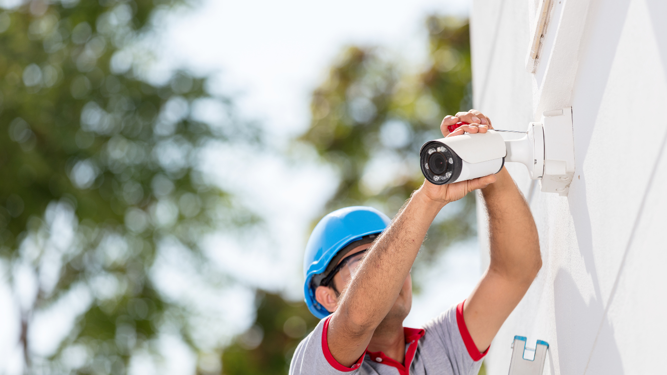 A man is installing a video surveillance camera on the side of a building.