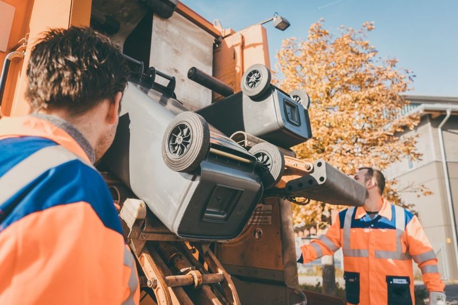 Workers inspect a large construction machine outdoors beside autumn trees and a truck.