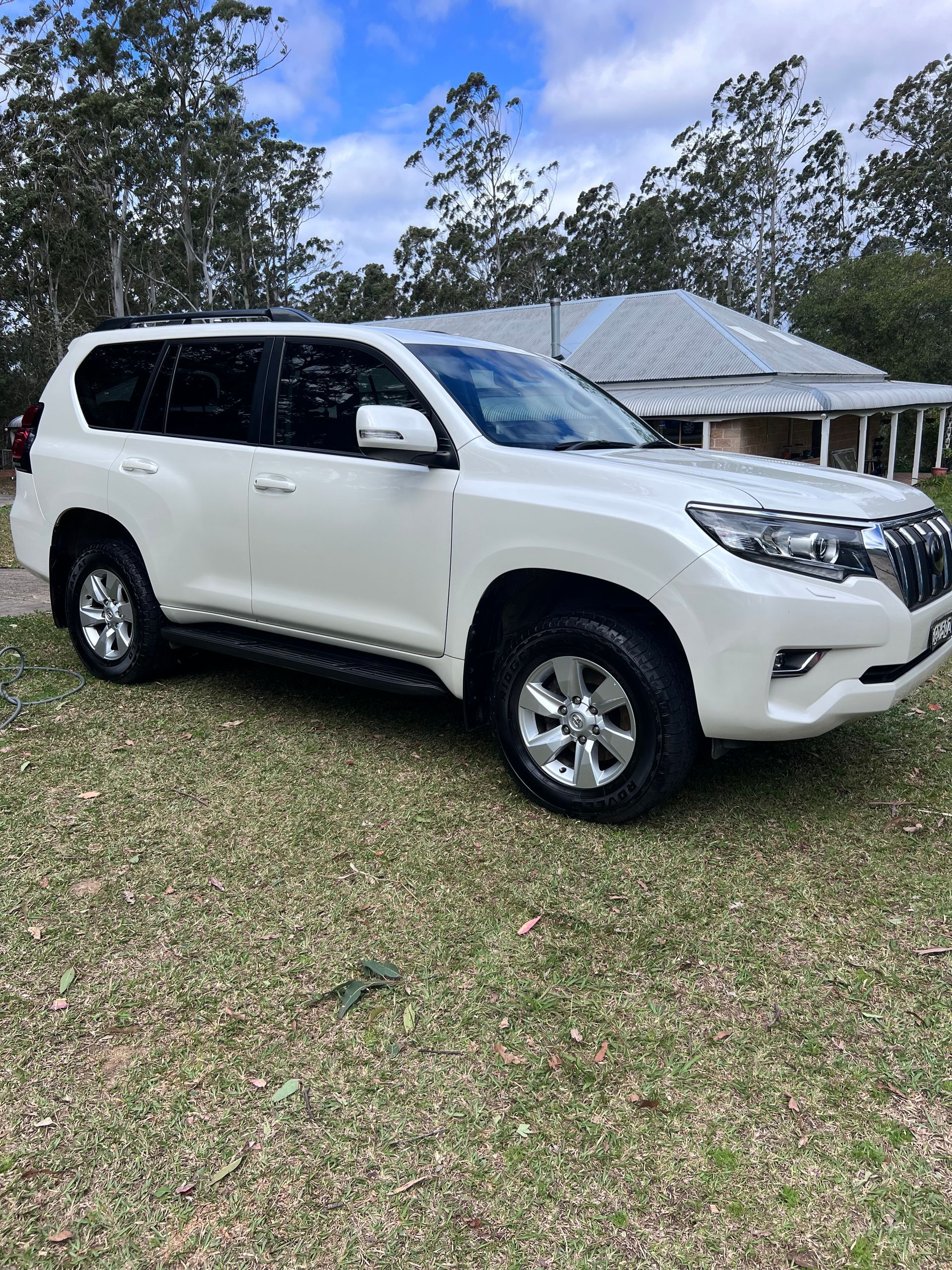 White SUV Parked On Grass In Front Of A House With Trees And A Cloudy Sky — Car Detailing Mobile Cleaning Co In Lake Cathie, NSW