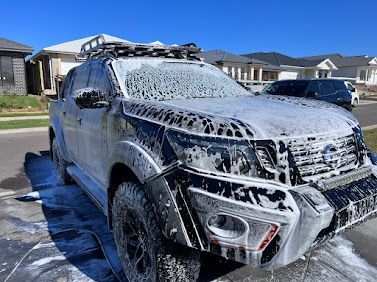 Black SUV And White Service Truck Parked On A Gravel Driveway With Water On The Ground — Car Detailing Mobile Cleaning Co In Port Macquarie, NSW