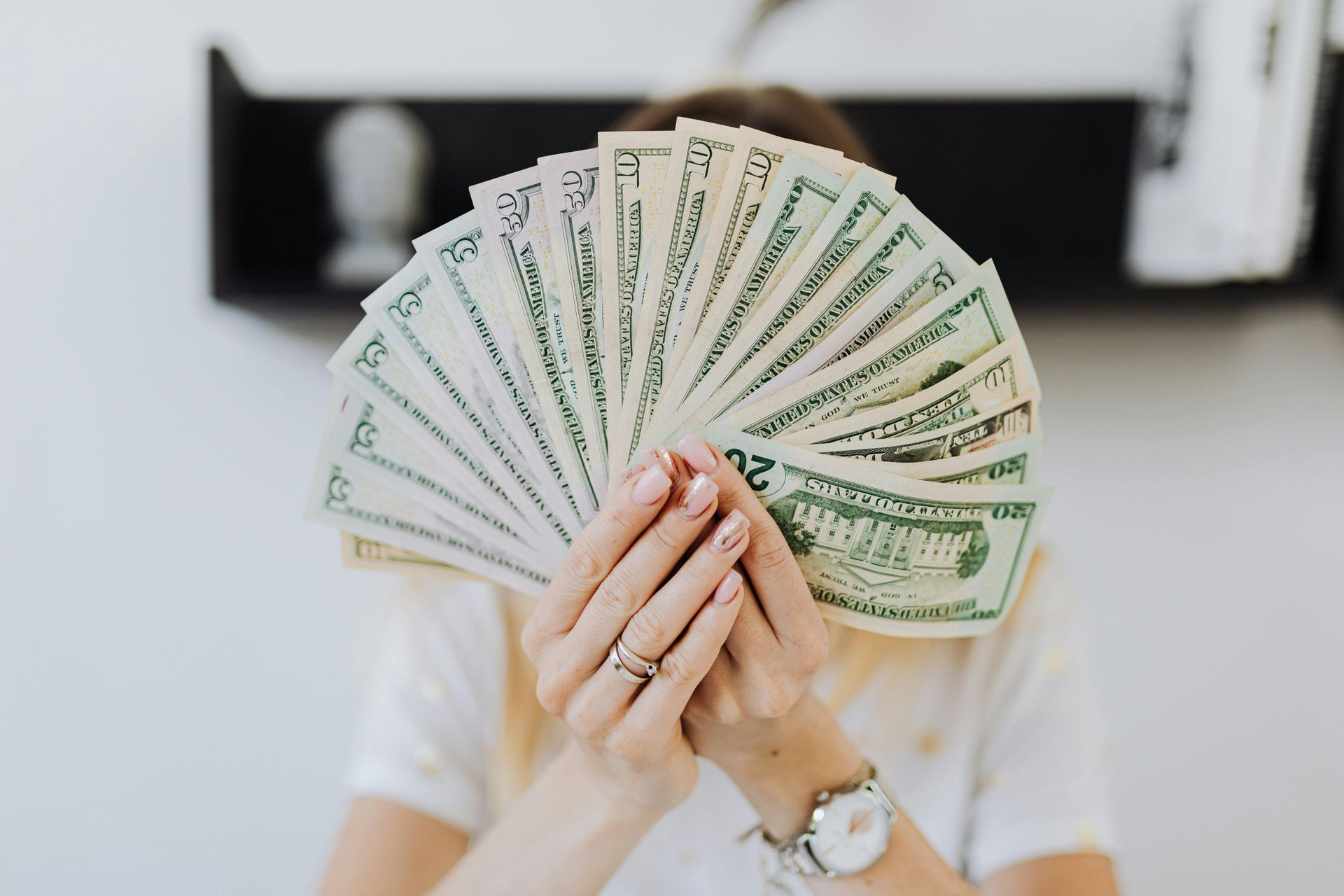 A person holds a fan of twenty-dollar bills in front of their face, obscuring their features.