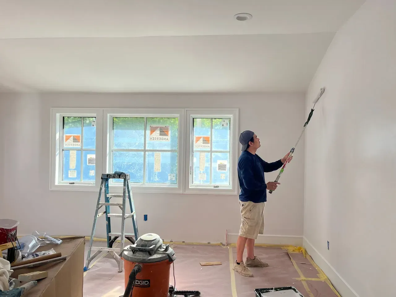 A man is painting a wall in a room with a roller.