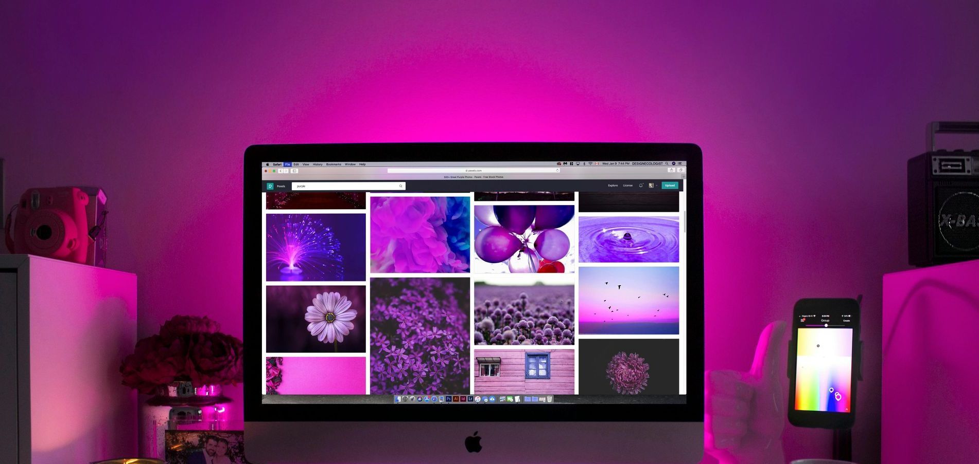 A computer monitor is sitting on a desk with purple lights behind it.