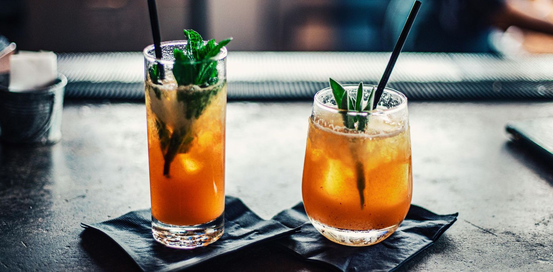 Two glasses of drinks with straws on a table.