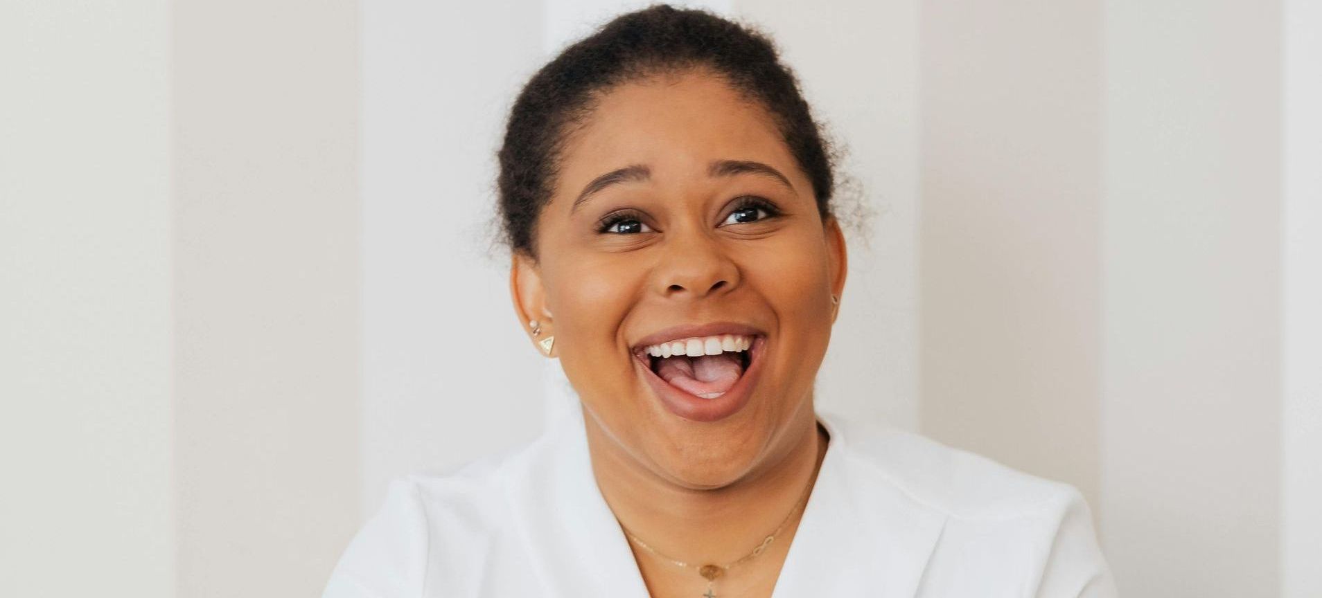 A woman in a white coat is laughing with her mouth open.