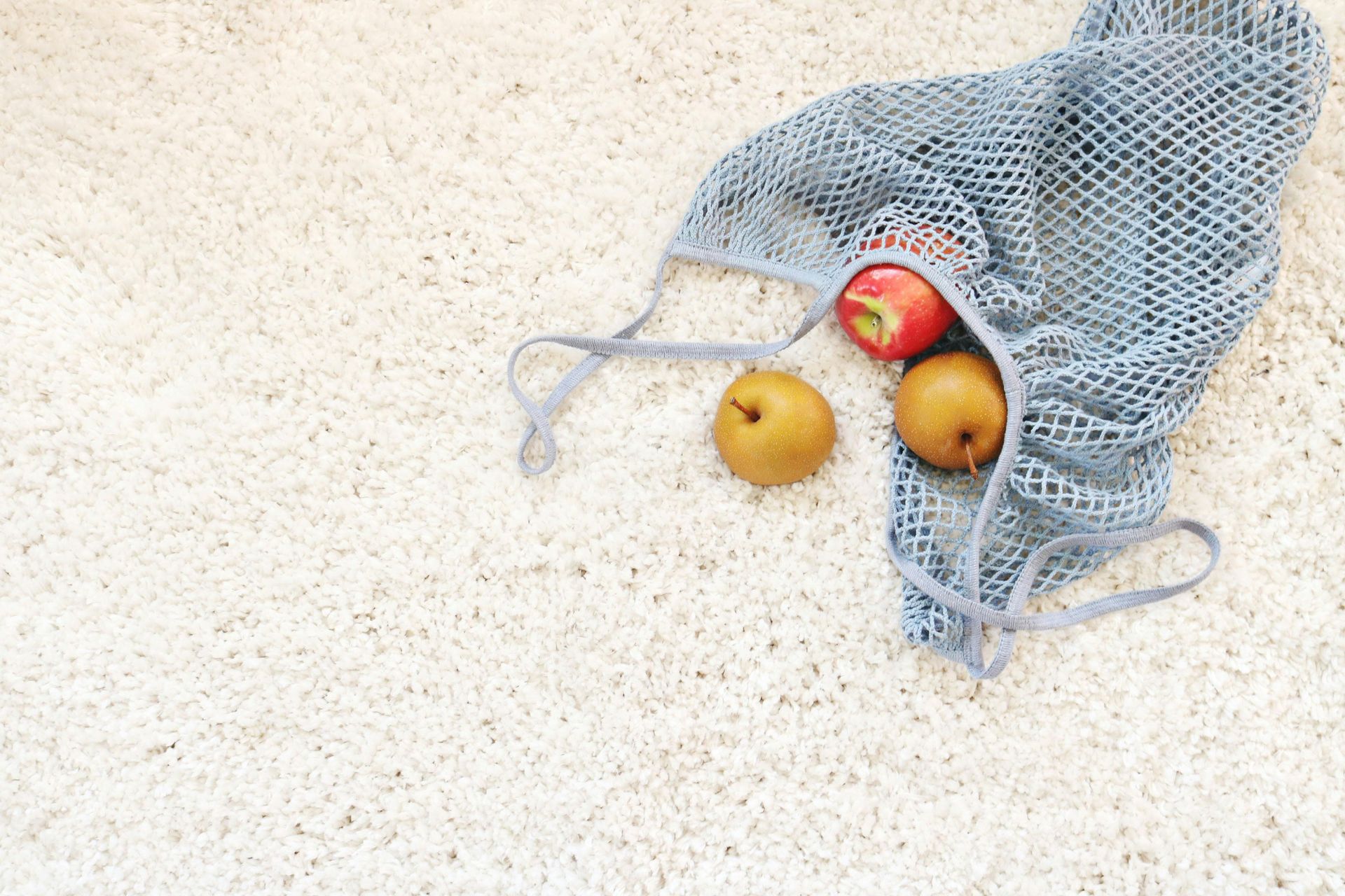 Mesh bag with apple and pears on a white, textured surface.