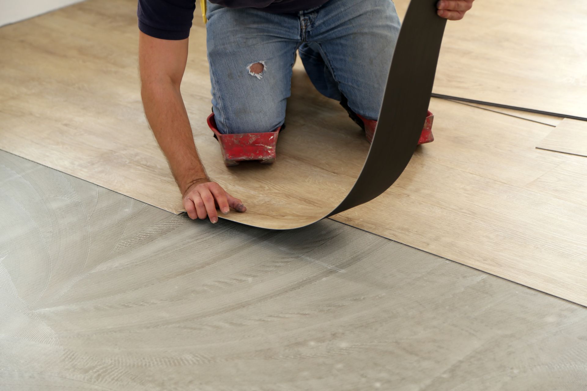Person installing flooring, peeling back a strip of dark material to reveal a new layer.