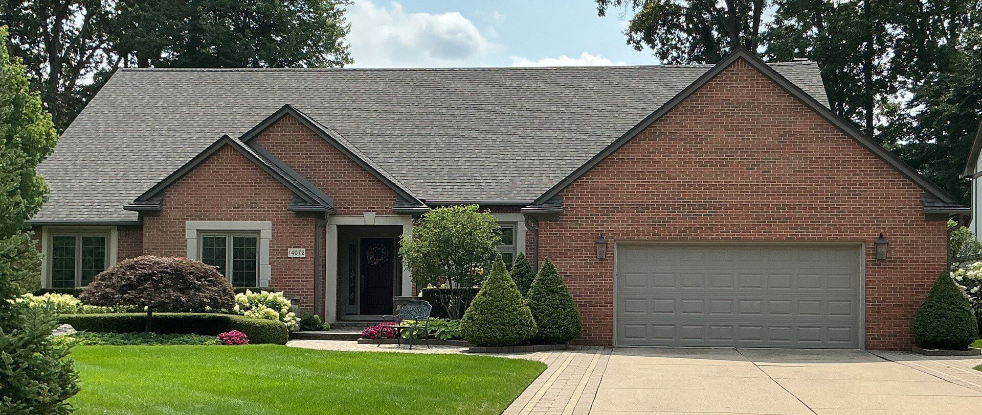 Brick suburban house with gray roof, two-car garage, and a green front lawn.