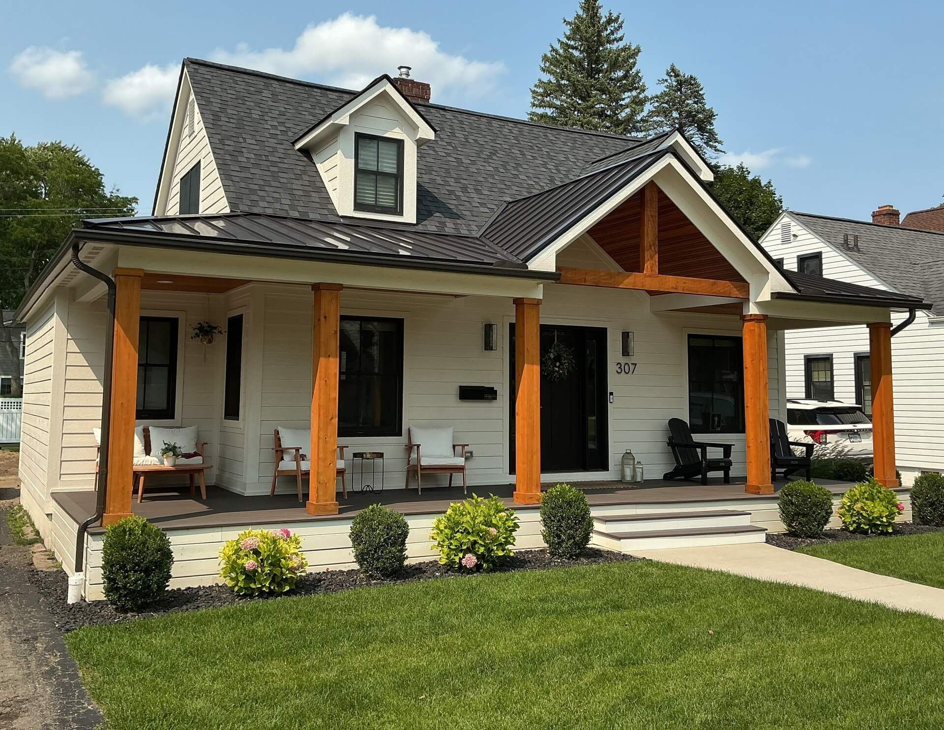 White house with stone columns, black roof, and front porch overlooking a green lawn.