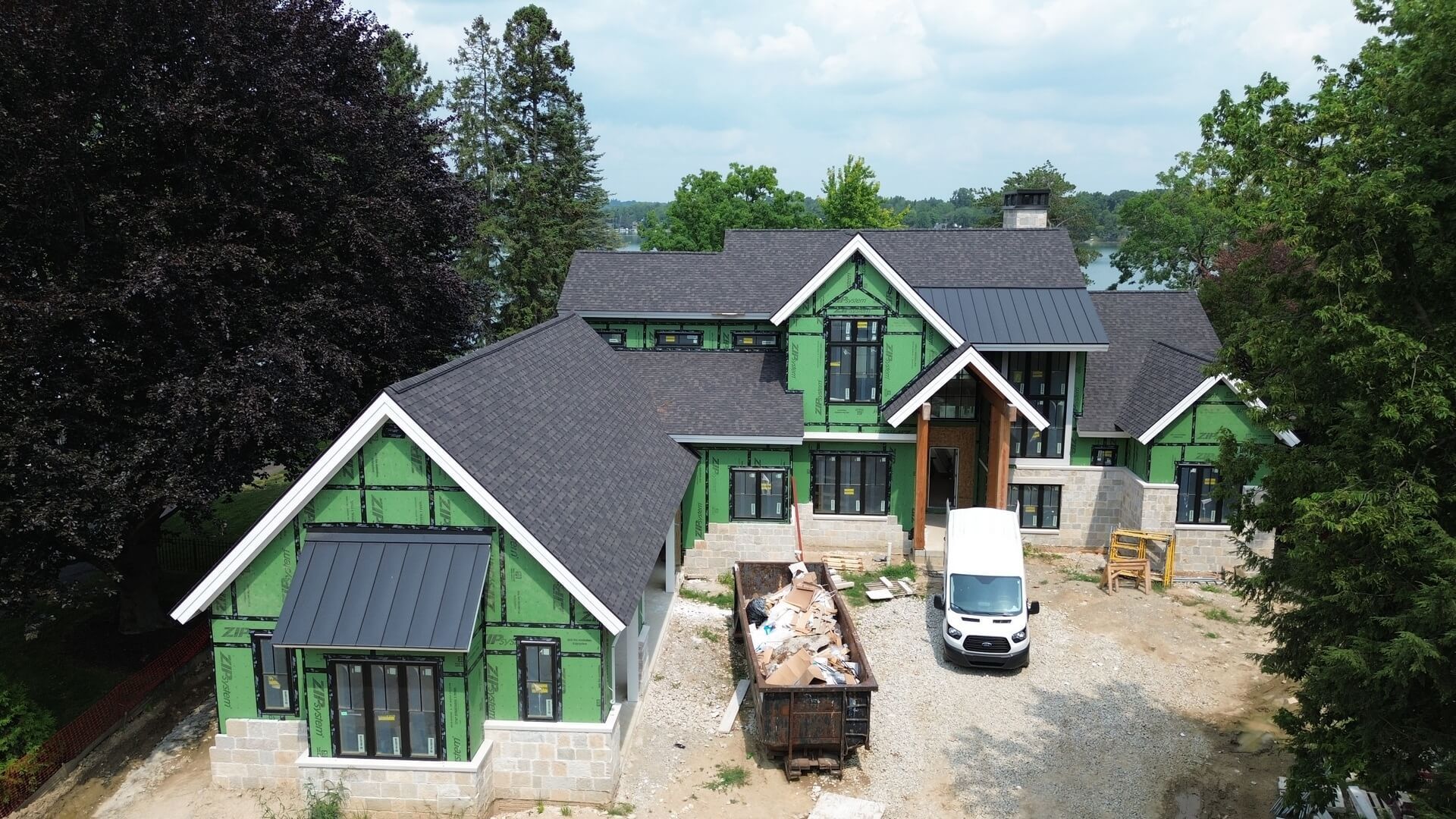 Aerial view of a large green-trimmed house with trucks and construction materials in the driveway.