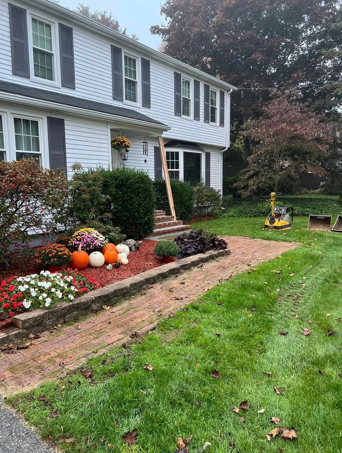 A two-story white house with a brick walkway and front yard landscaping featuring colorful fall flowers and pumpkins. A two-story white house with a brick walkway and front yard landscaping featuring colorful fall flowers and pumpkins.