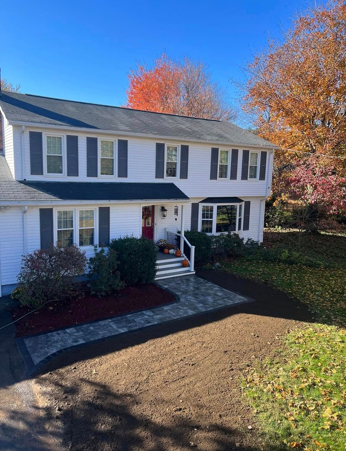 A two-story white house with a brick walkway and front yard landscaping featuring colorful fall flowers and pumpkins. A two-story white house with a brick walkway and front yard landscaping featuring colorful fall flowers and pumpkins.