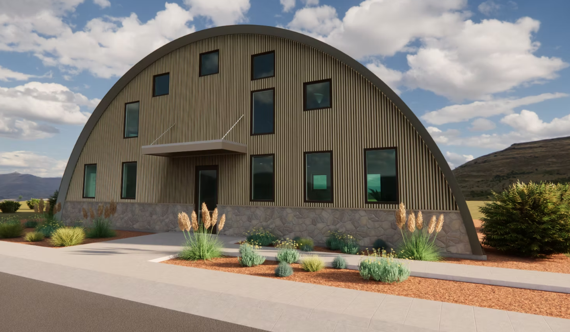 Curved tan building with arched roof, blue windows, and desert landscaping under a partly cloudy sky