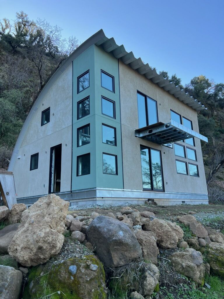 A house with a lot of windows is sitting on top of a rocky hillside.